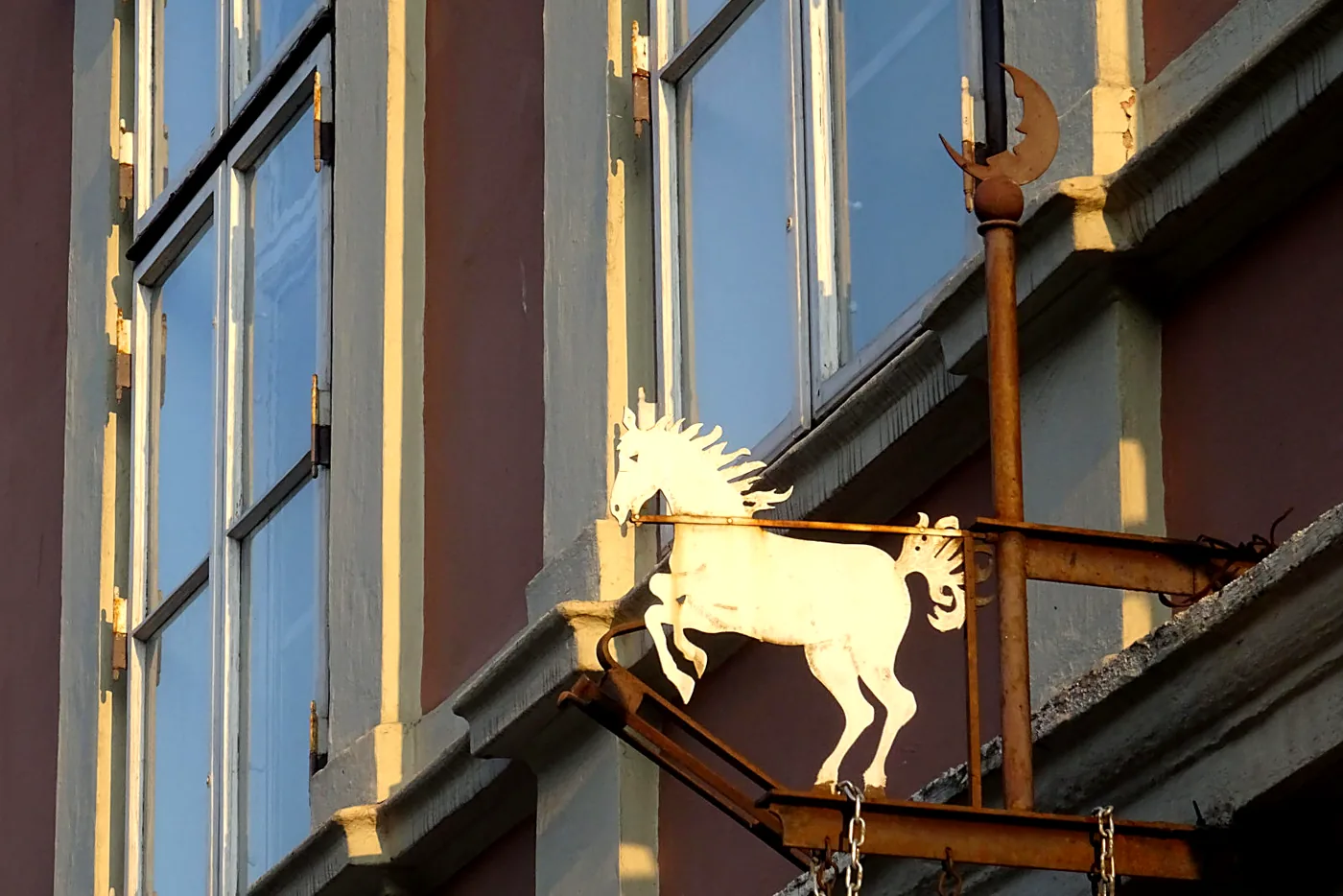 Schmiedeeisernes Aushängeschild mit weißem Pferd und Halbmond an der Fassade